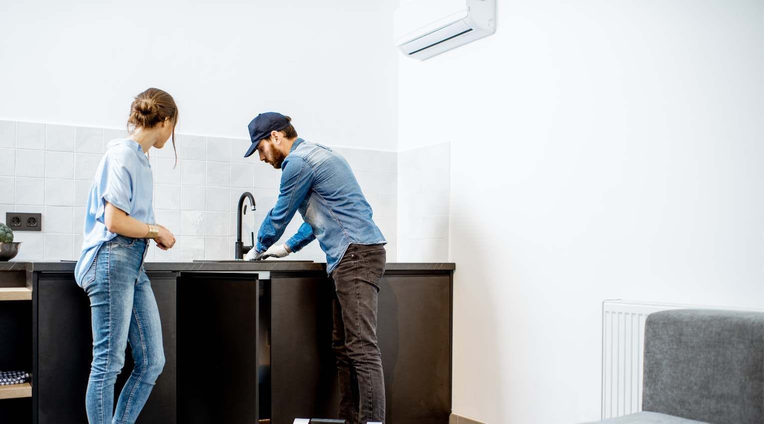 plumber fixing sink, female homeowner watching 